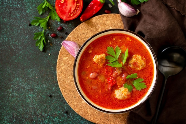 Tomato soup with meatballs and chili peppers on a dark stone or slate table Top view flat lay