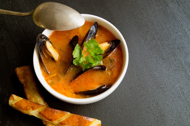 Tomato soup with mussels. With fried croutons on a black background.