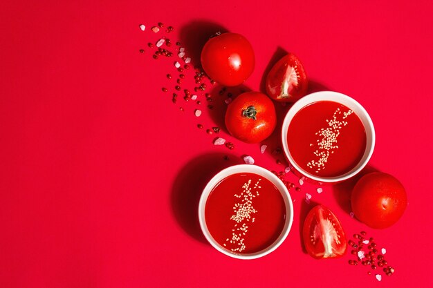 Tomato soup with sesame seeds in bowls on a red background. Ripe vegetables, rose Himalayan salt, pink peppercorn. A modern hard light, dark shadow, top view