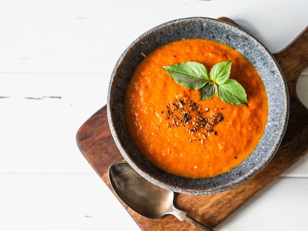 Tomato soup with spices and fresh basil on a white wooden background. 