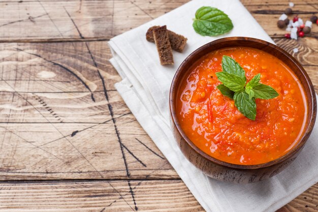 Tomato soup in a wooden bowl with pieces of toast on a rustic table