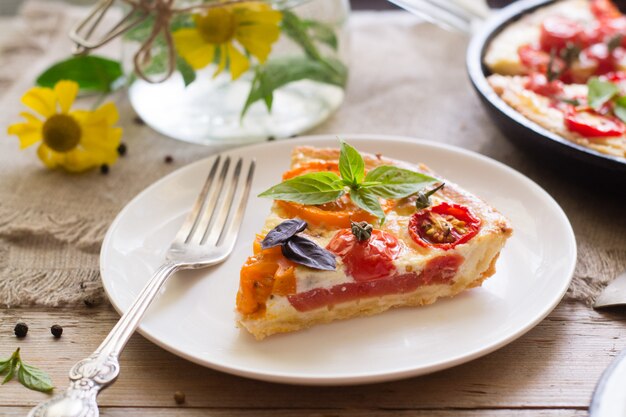 Tomato tart made with shortcrust  pastry, red and yellow tomatoes, cheese and cream. Concept of healthy eating or vegetarian food on rustic wooden background