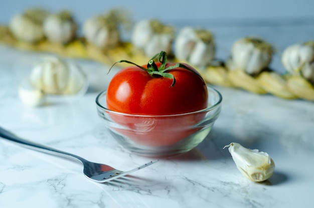 Tomato and white garlic cloves on a white table