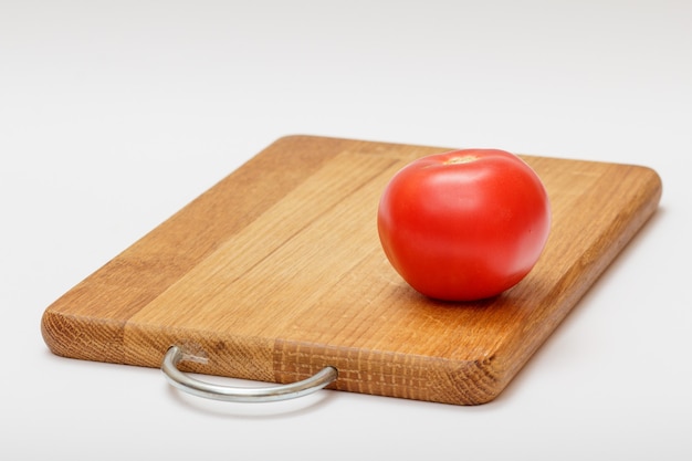 Tomato on wooden cutting board on white background. Ingredients for vegetarian food.