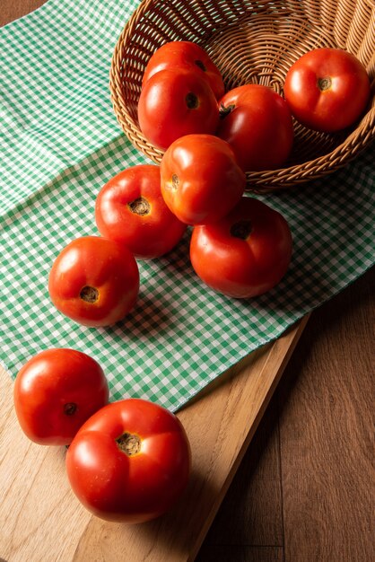 Tomatoes arranged in a basket on a checkered table cloth and on a wood table