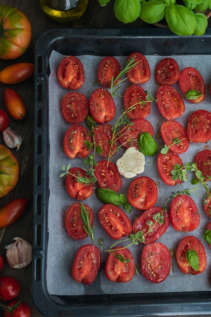 Tomatoes on baking sheet, aromatic herbs, thyme, basic, garlic and olive oil