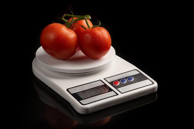 Tomatoes, beautiful tomatoes placed on a precision scale on black background, selective focus.