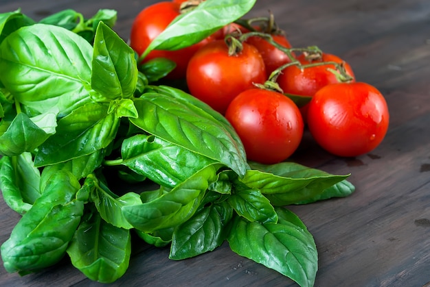 Foto pomodori e grappolo di basilico fresco verde su uno sfondo di legno scuro,