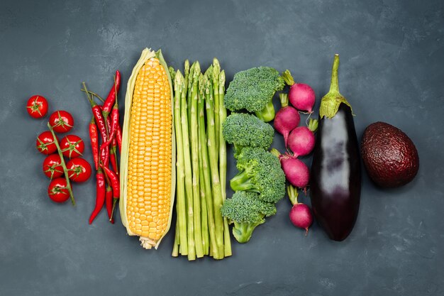 Tomatoes, chili peppers, corn, asparagus, broccoli, radishes, eggplant and avocado are lined up on black concrete