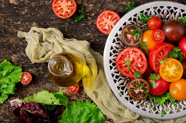 Pomodori di diversi colori con erbe verdi in una ciotola su uno sfondo nero.