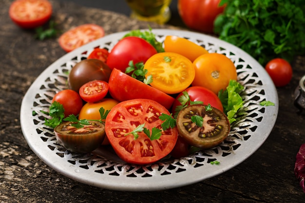 Tomatoes of different colors with green herbs in a bowl on a black table