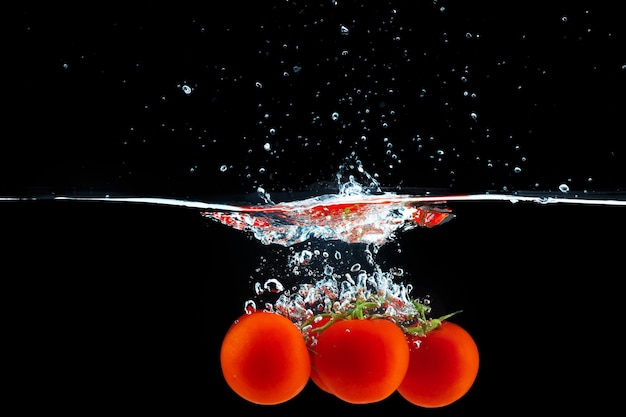 Tomatoes falling into the water with a splash against black