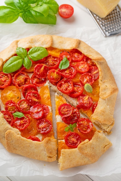 Tomatoes galette or pie with cheese and herbs on a white wooden background Vegetarian dish