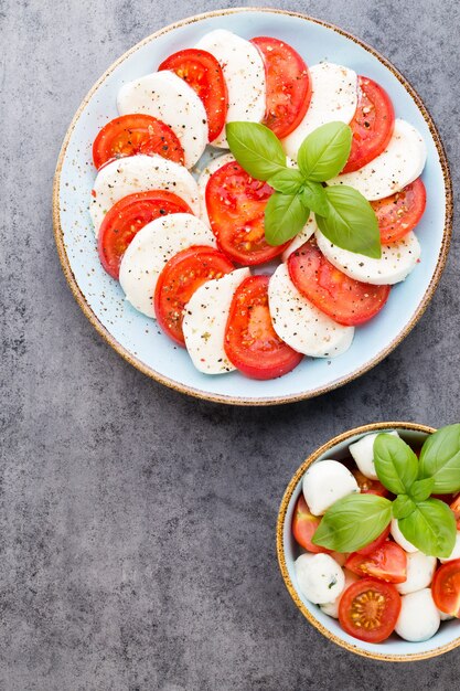 Tomatoes, mozzarella cheese, basil and spices on gray slate stone chalkboard. Italian traditional caprese salad ingredients. Mediterranean food.