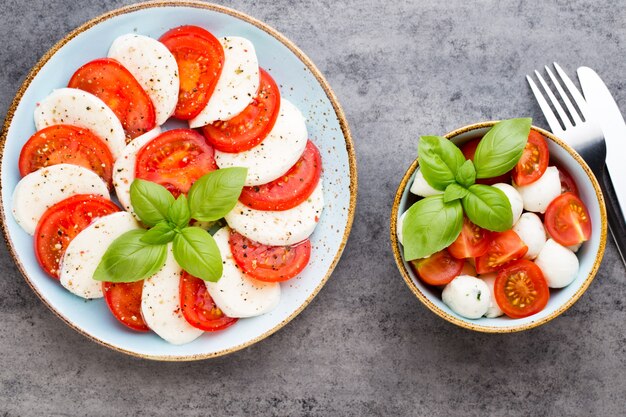 Tomatoes, mozzarella cheese, basil and spices on gray slate stone chalkboard. Italian traditional caprese salad ingredients. Mediterranean food.