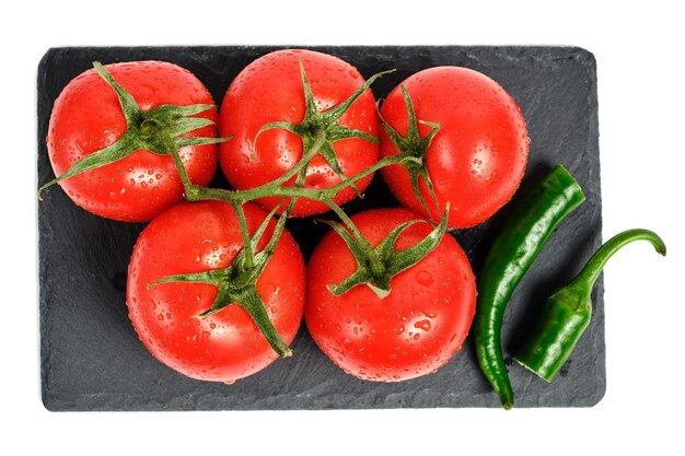 Tomatoes and pod of hot pepper on slate cutting board isolated white background