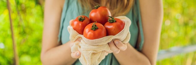 Photo tomatoes in a reusable bag in the hands of a young woman zero waste concept banner long format