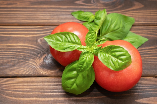 Foto pomodori con basilico su un fondo di legno. composizione degli alimenti. vista dall'alto