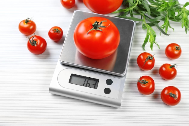 Tomatoes with digital kitchen scales on wooden background