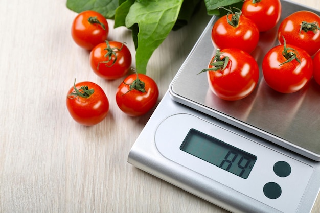 Tomatoes with digital kitchen scales on wooden background