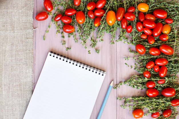 Pomodori con spezie e un libro di ricette sulla tavola di legno. vista dall'alto.