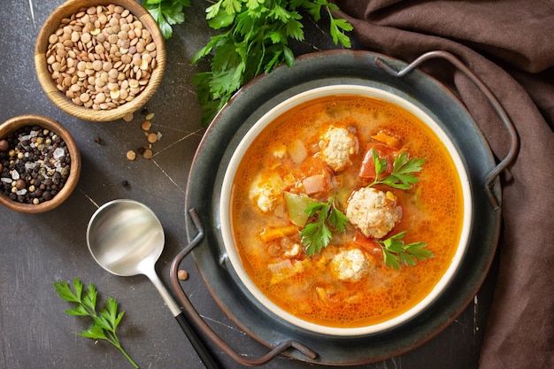 Tomatolentil soup with meatballs and vegetables on a dark slate table top Top view