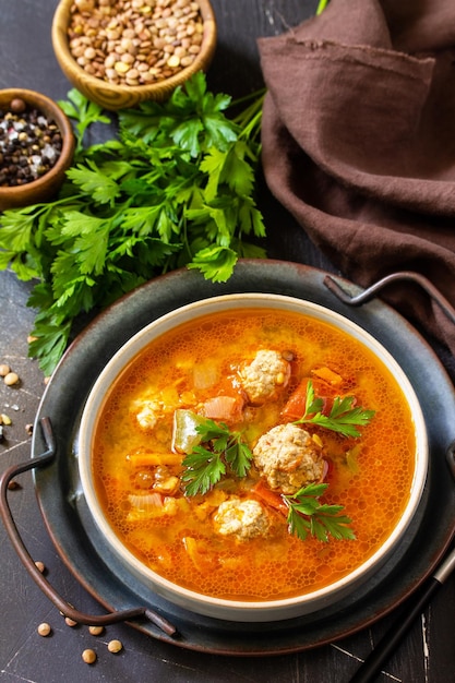 Tomatolentil soup with meatballs and vegetables on a dark slate table top