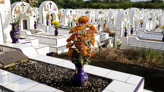 묘지나 묘지에 있는 흰색 도자기 무덤에 있는 꽃병에 묘비와 꽃