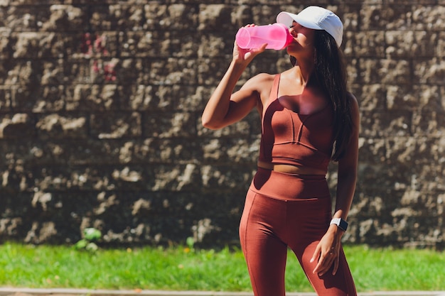 Pancia tonica e forma snella di donna atletica, con in mano una bottiglia d'acqua e indossa un braccialetto