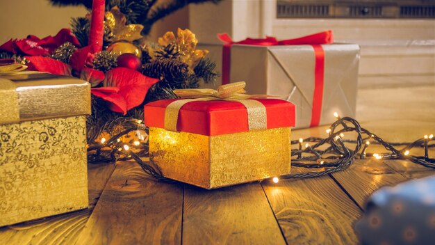 トーンのクリスマスの背景。リビングルームの木製の床に金色のギフトボックス、花輪、光るライト