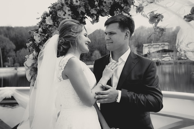 Toned monochrome portrait of happy bride and groom looking at each other under arch