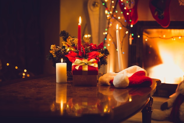 Toned photo of burning candles, fireplace and giftbox at christmas eve