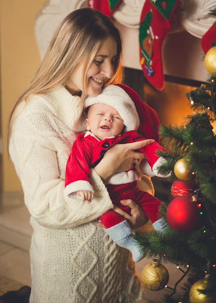 산타 의상에 작은 아들의 몸매 사진과 크리스마스 트리에서 포즈 웃는 어머니