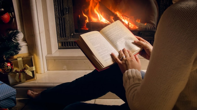 Foto tonica di una donna che legge un libro accanto al caminetto e al caminetto acceso