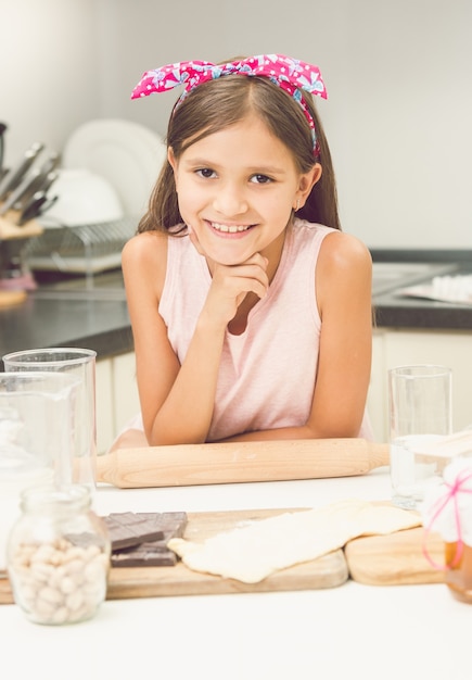 Toned portrait of cute smiling girl posing on kitchen while making dough