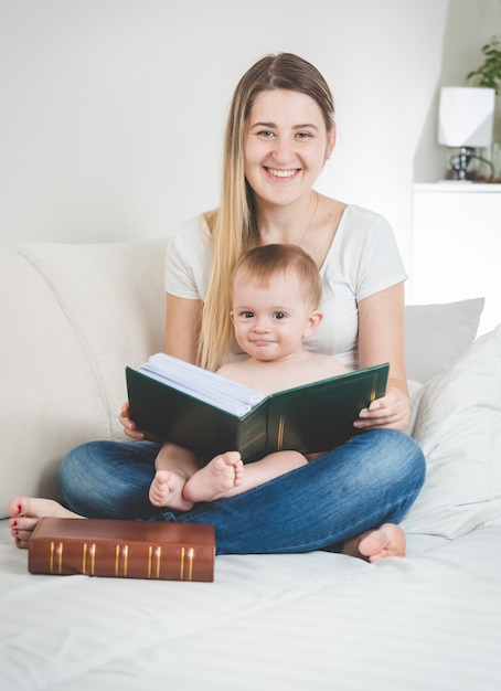 Ritratto tonico di giovane madre felice e del suo bambino che posano con il grande libro