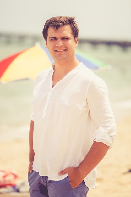 toned portrait of smiling handsome man posing on beach at sunny day