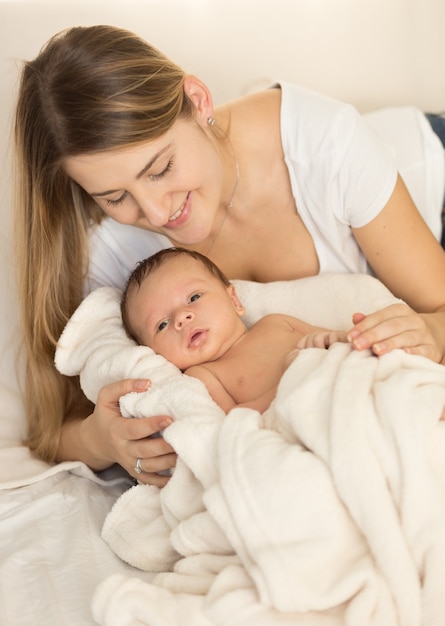 Toned portrait of young caring mother hugging newborn baby on bed