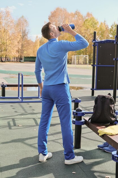 Foto uomo magro e tonico di mezza età che beve un cocktail di proteine del siero di latte da uno shaker sportivo utilizzando bevande proteiche per un adeguato aumento di peso e muscoli forti bevanda sportiva allenamento all'aperto nella stagione autunnale