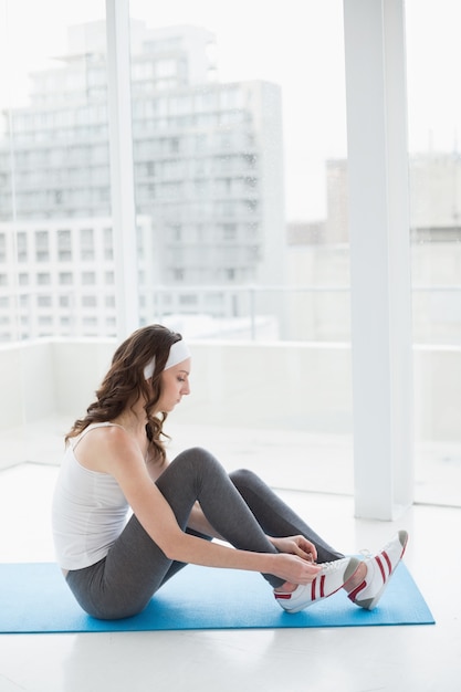 Toned woman wearing shoes on exercise mat at fitness studio