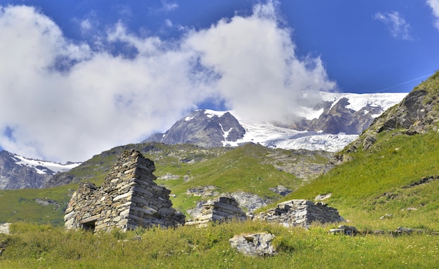 Toneellandschap van berg met ruïnes op een weide en gletsjerachtergrond