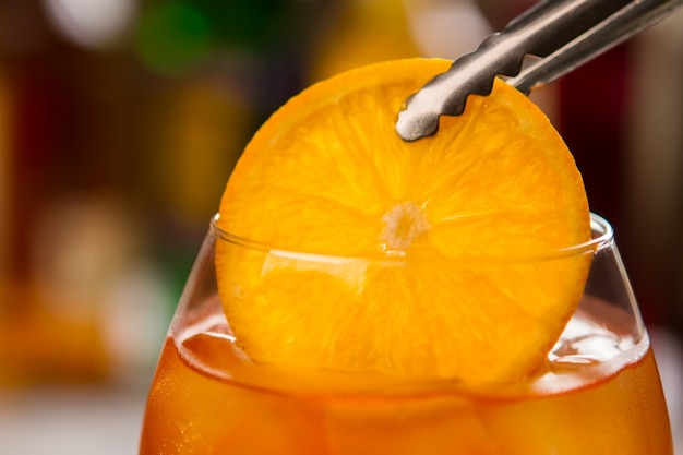 Photo tongs with slice of orange. glass filled with drink. cool alcoholic beverage. have you tried aperol spritz.