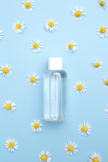 Tonic water with floral extracts for skincare Nature cosmetics in glass bottle with pipette and chamomile flowers on blue background Face and body care spa concept