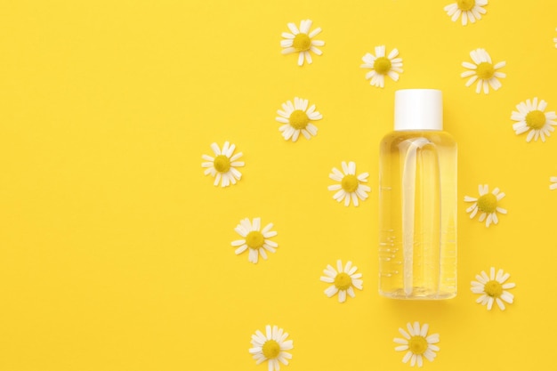 Tonic water with floral extracts for skincare Nature cosmetics in glass bottle with pipette and chamomile flowers on yellow background Face and body care spa concept