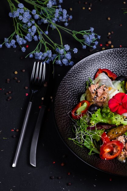 Tonijnsalade in combinatie met gebakken aardappelen, paprika, olijven, gepocheerd ei, op een kussen met slamix en dressing op basis van twee mosterdsoorten, op een donkere ondergrond