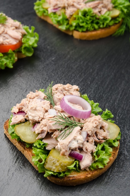 Tonijnsandwiches met sla, tomaten, augurken en uien op leisteen