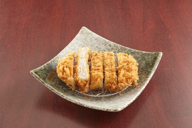 Tonkatsu는 싱가포르 음식의 나무 테이블 배경 측면에서 분리된 접시에 제공됩니다.