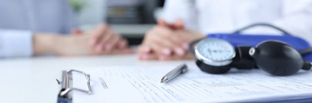 Tonometer and clipboard with medical history lying on table near doctor and patient pregnancy