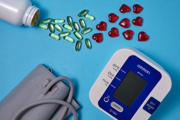 Tonometer yellow vitamin E capsules and red glass hearts are scattered on a blue background Vitamin supplements to combat hypertension and atherosclerosis