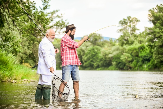 Pescatori felici troppo occupati buon profitto amici uomini con canna da pesca e rete avventure di pesca a mosca hobby di uomo d'affari pensionamento pesca papà in pensione e figlio barbuto maturo